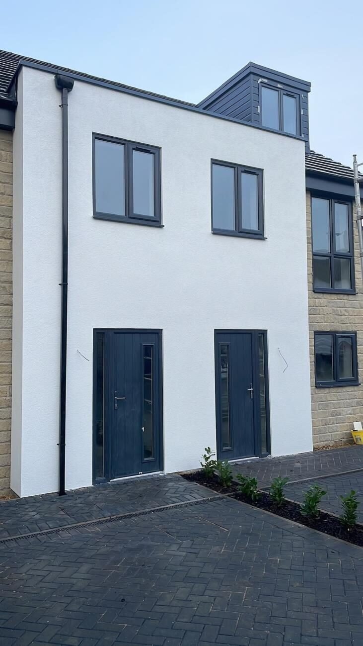 Tall white rendered townhouse with grey door and block-paved drive